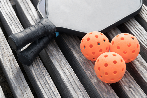 two-pickleball-paddles-and-three-pickle-balls-on-wooden-bench