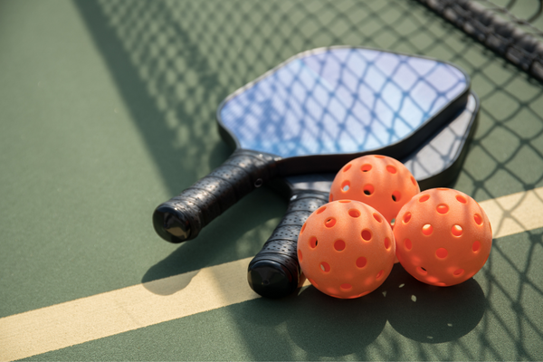 two pickleball paddles with three pickleballs on the court